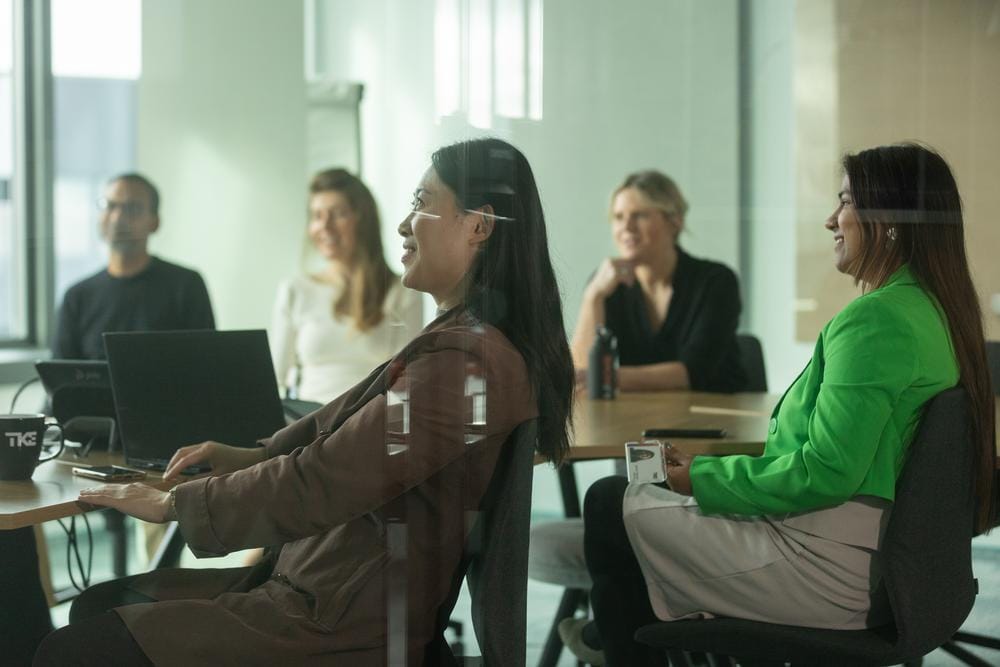 Des collègues souriants réunis autour d’une table de réunion avec leurs ordinateurs portables.